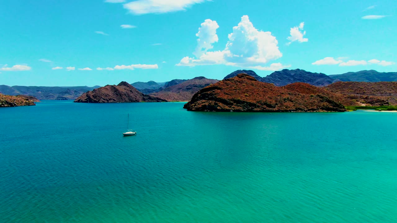 Sailboat below rocky island in bright turquoise bay