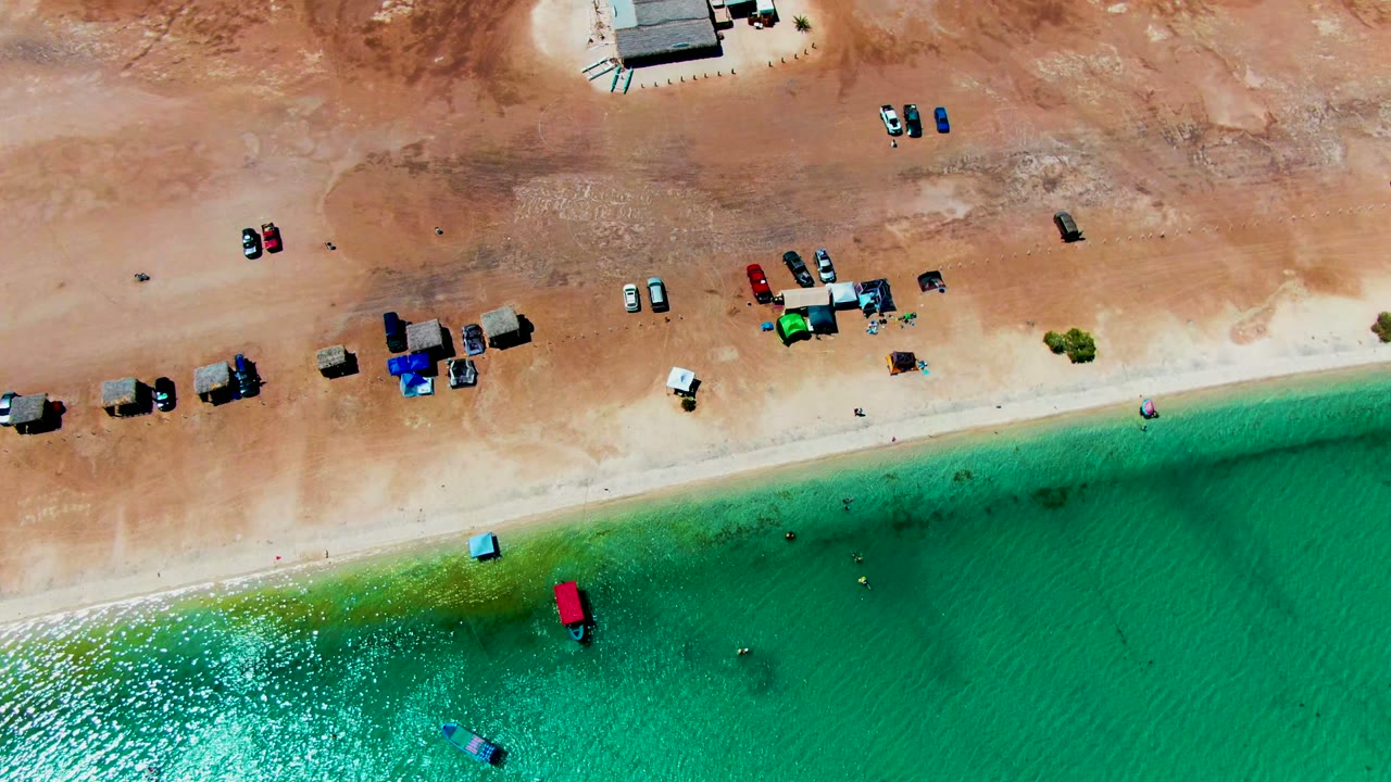 Aerial beach frame with vehicles on sand and small waves along the shore.