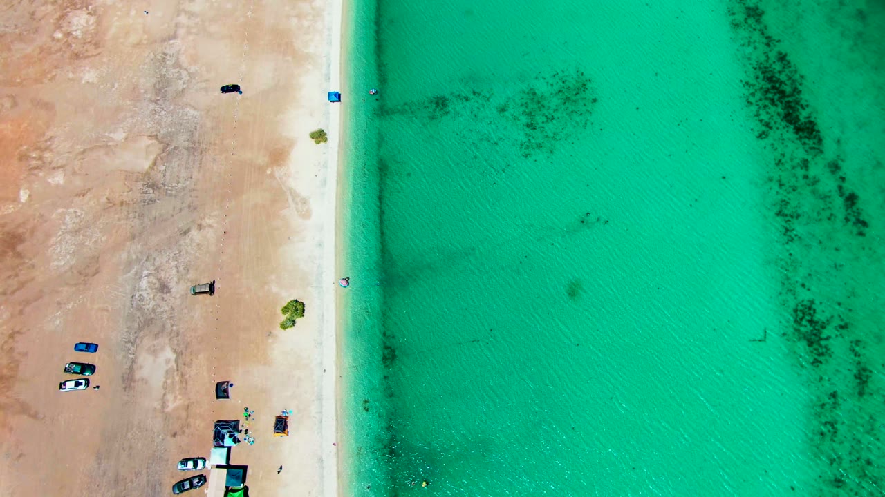 Aerial beach view with vehicles on sand and clear water beside the shoreline.
