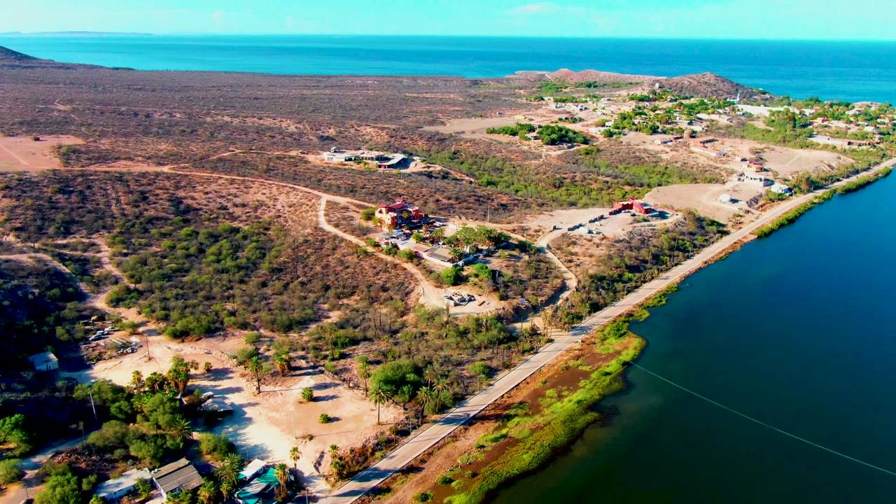 High aerial view of road, lagoon water, desert brush, and scattered buildings.