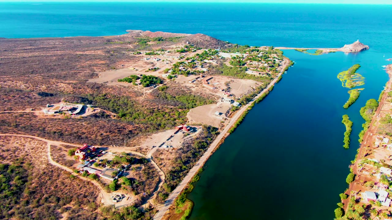Drone view of shoreline traffic corridor with homes, desert terrain, and water.