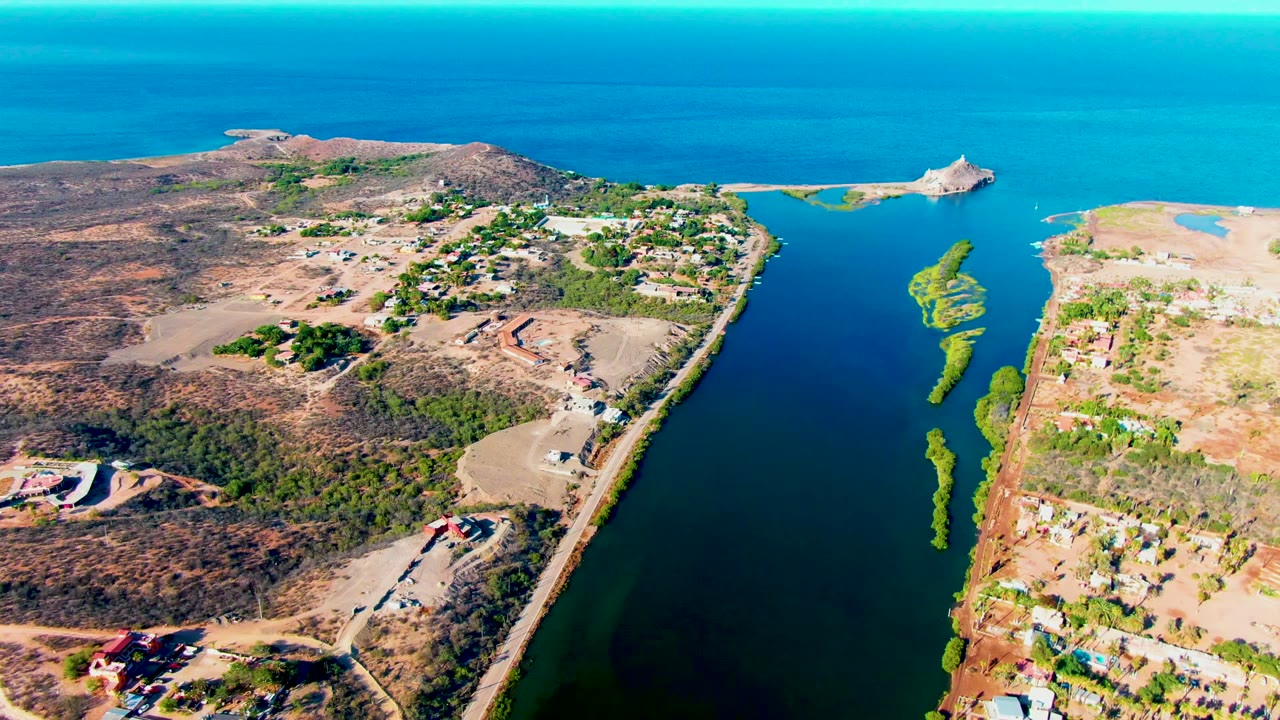 High aerial view of a canal-like waterway, road, buildings, and ocean.