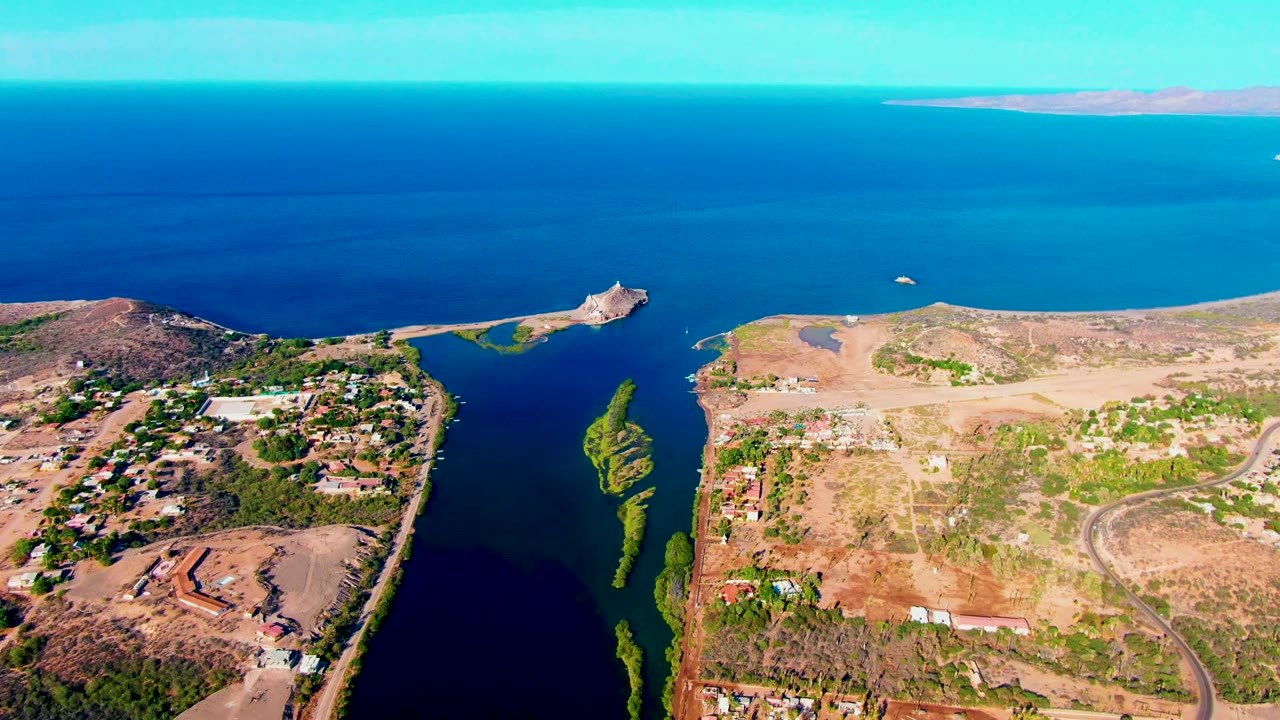 Aerial coastal view with a narrow waterway, green vegetation strips, roads, and open sea.