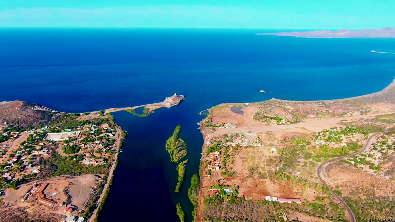 Wide aerial view of the channel, small island, shoreline roads, and distant ocean.