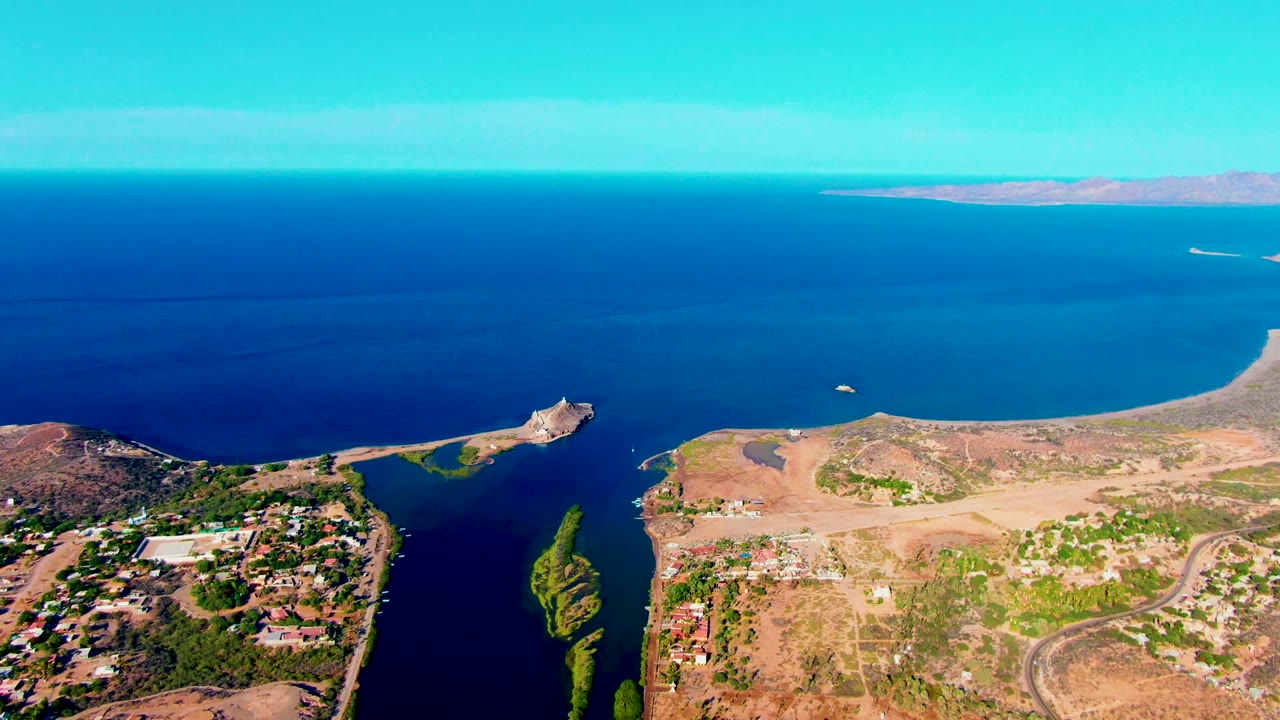 Aerial coastline with dry land, buildings, inlet, ocean, and clear sky