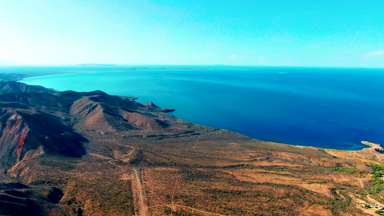 Drone view of coastal hills, dirt road, and open water