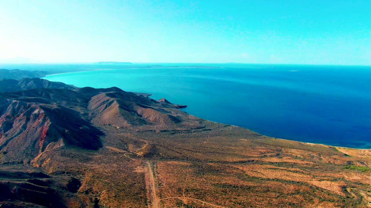 Wide drone view of desert hills dropping toward blue water