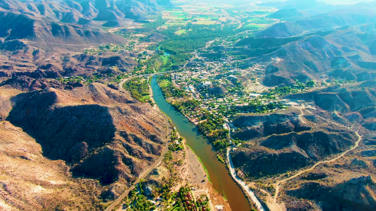 Aerial valley view with river, settlement, roads, and dry mountains.