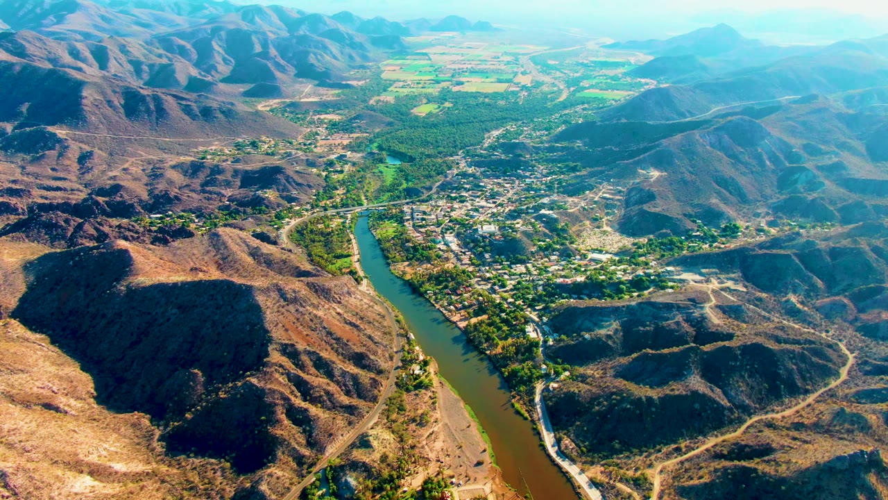 High aerial view of river bend, town buildings, and arid hills.