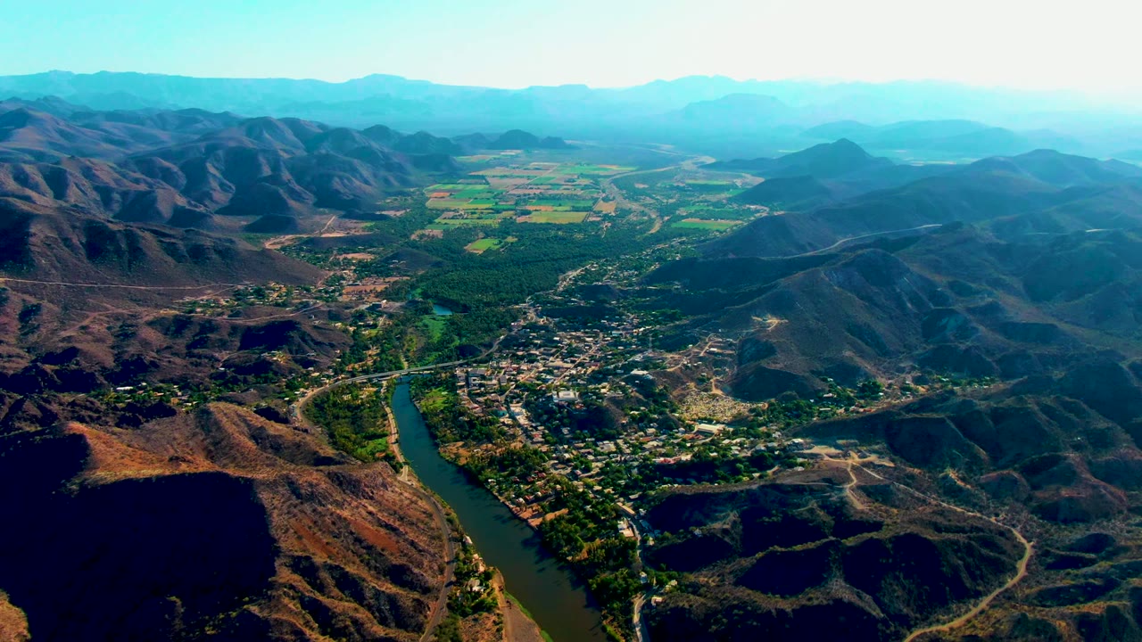Wide aerial valley view with river and settlement below.