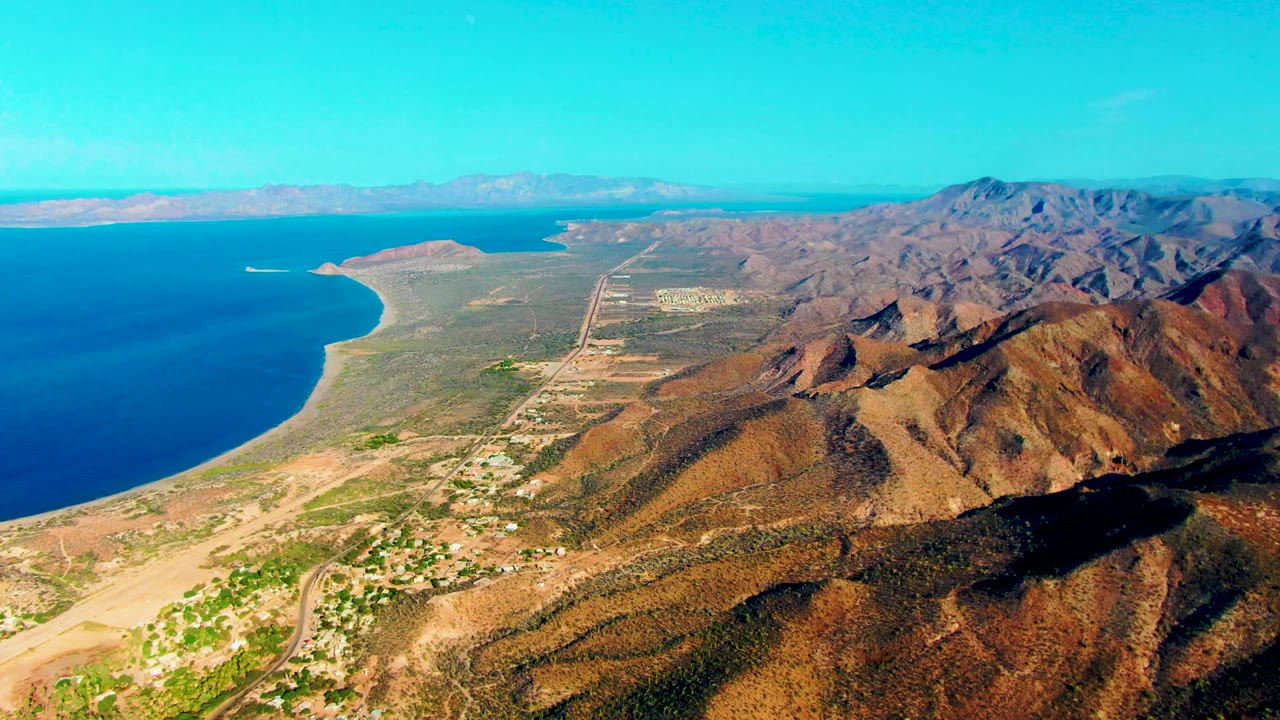 Wide aerial view of coastal desert terrain, ocean, mountains, and airport runway.