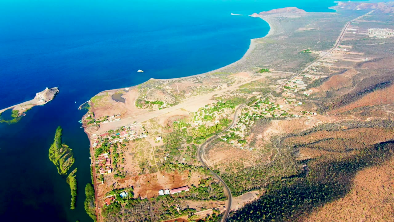 Aerial shoreline with inlet, breakwater, beach, town edge, roads, and hills.