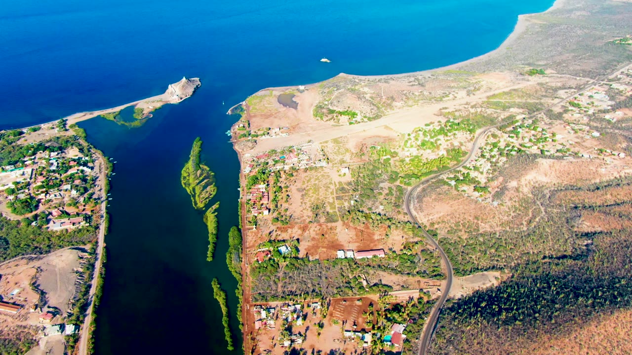 Drone view of blue water, shoreline land, roads, and small building clusters.