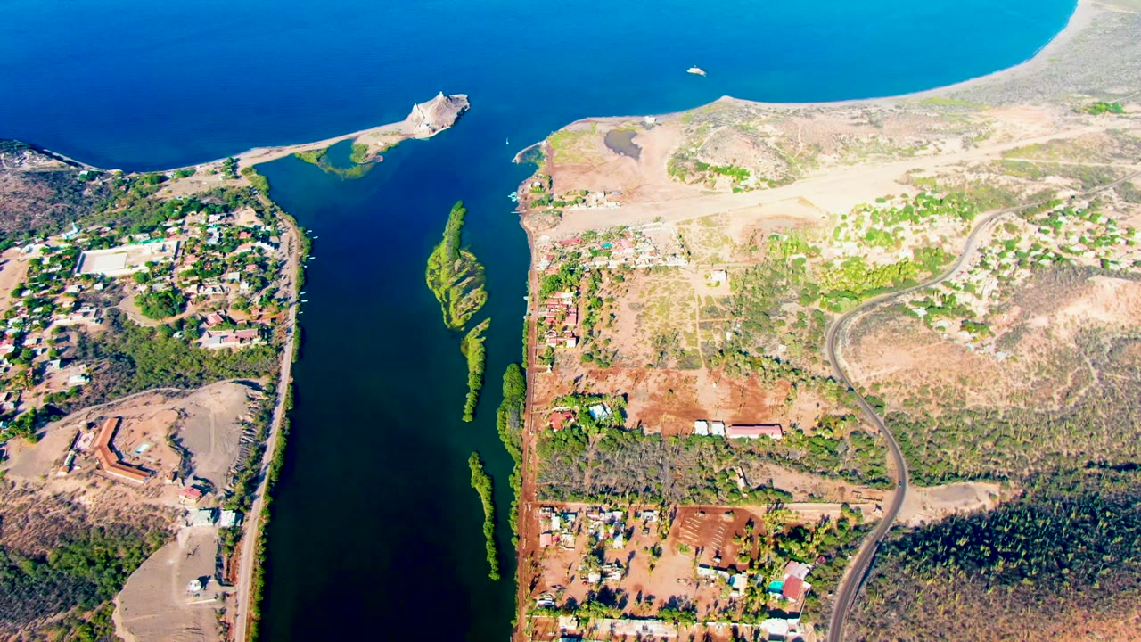 Aerial view of the channel with ocean beyond, dry shore, roads, buildings, and green vegetation.