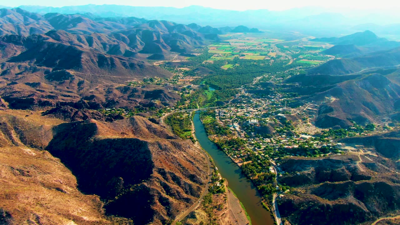 High aerial view of a river, settlement, hills, and green fields.