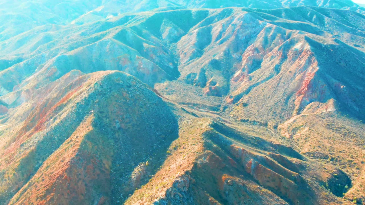 Aerial view over Mulege, Baja California Sur mountain ridges with red-brown slopes, green scrub, dry valley cuts, and no visible people.