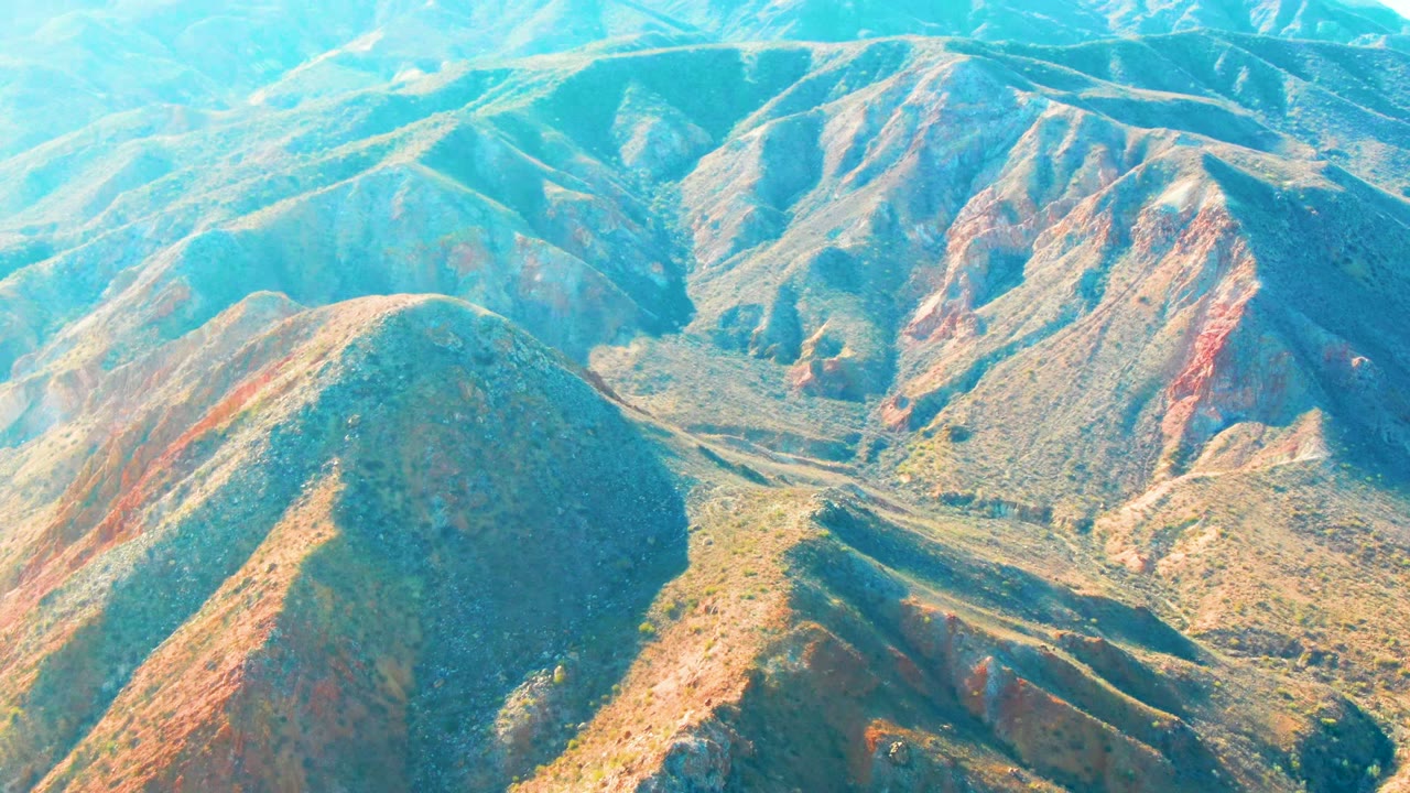 Layered mountain slopes with red exposed earth and green scrub seen from above.