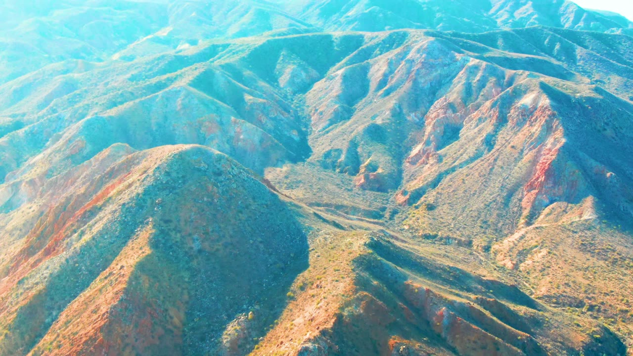 Mid-clip aerial frame over Mulege, Baja California Sur with a rounded foreground ridge, branching dry washes, distant slopes, and no visible people.