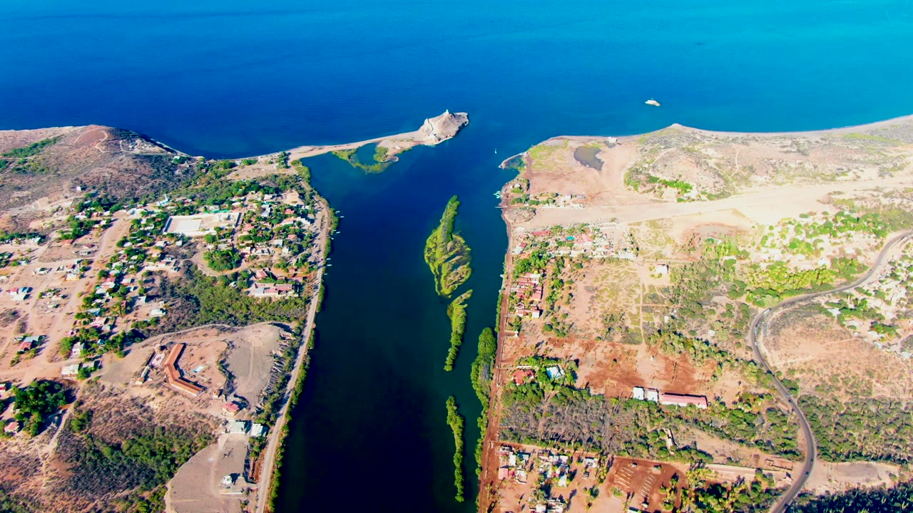 Drone view of waterway, shoreline, buildings, roads, and dry terrain.