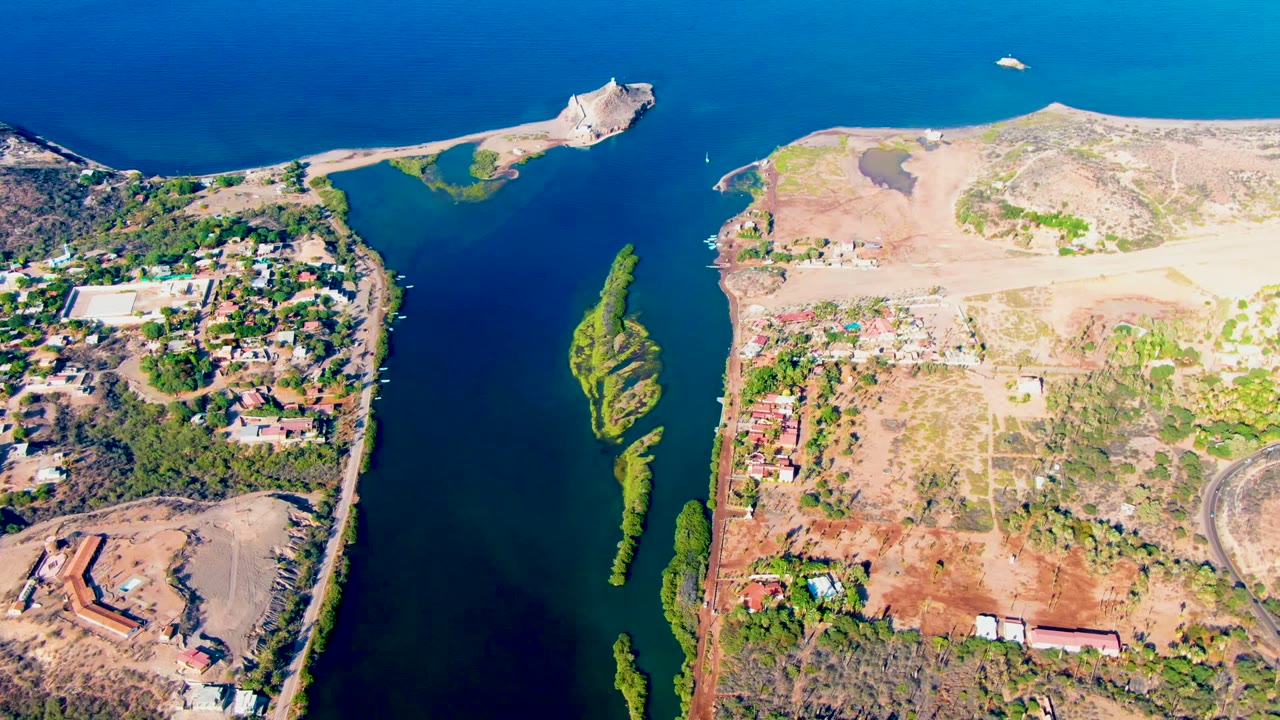 Overhead view of the channel with sandy flats, buildings, and green patches along both shores.