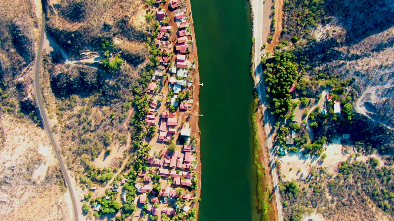Green river beside roadside houses and dry terrain.