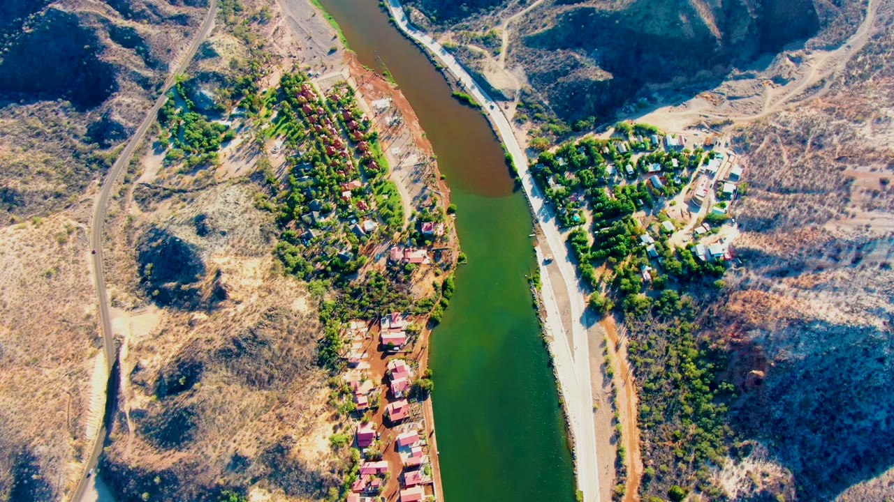 Overhead view of river bend, roadside, dry hills, and small settlement.