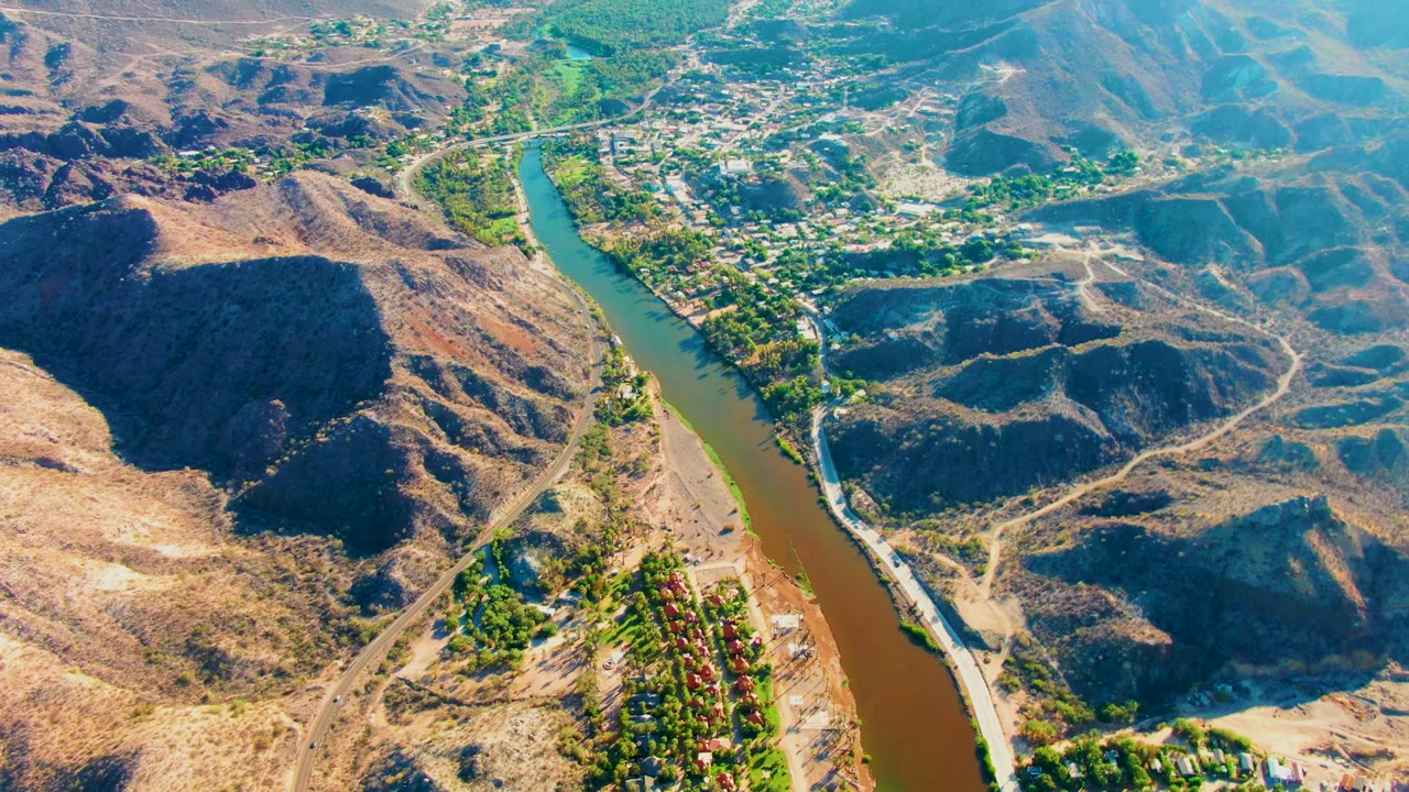 High drone view of the river bending past hills and a small town area.