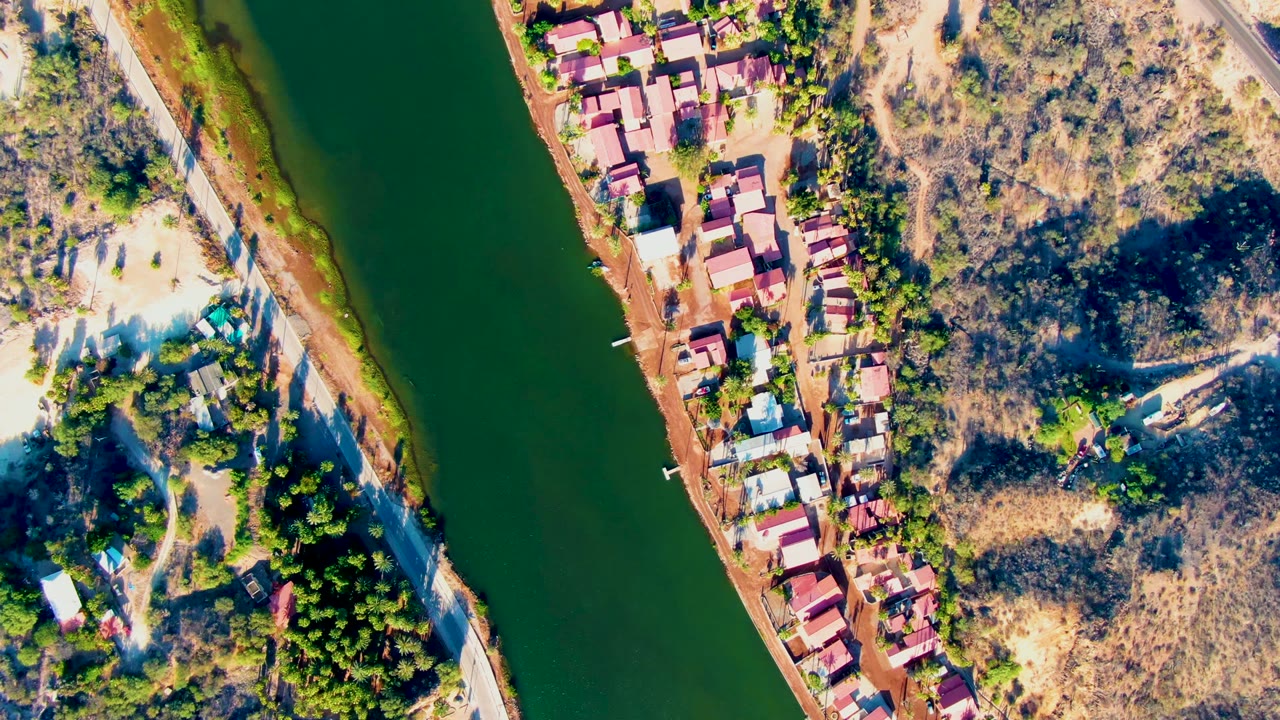 Overhead riverbank with clustered red roofs, road, trees, and dry land.