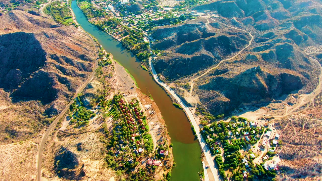 Aerial river bend with dry hills, roads, trees, and buildings along the water.