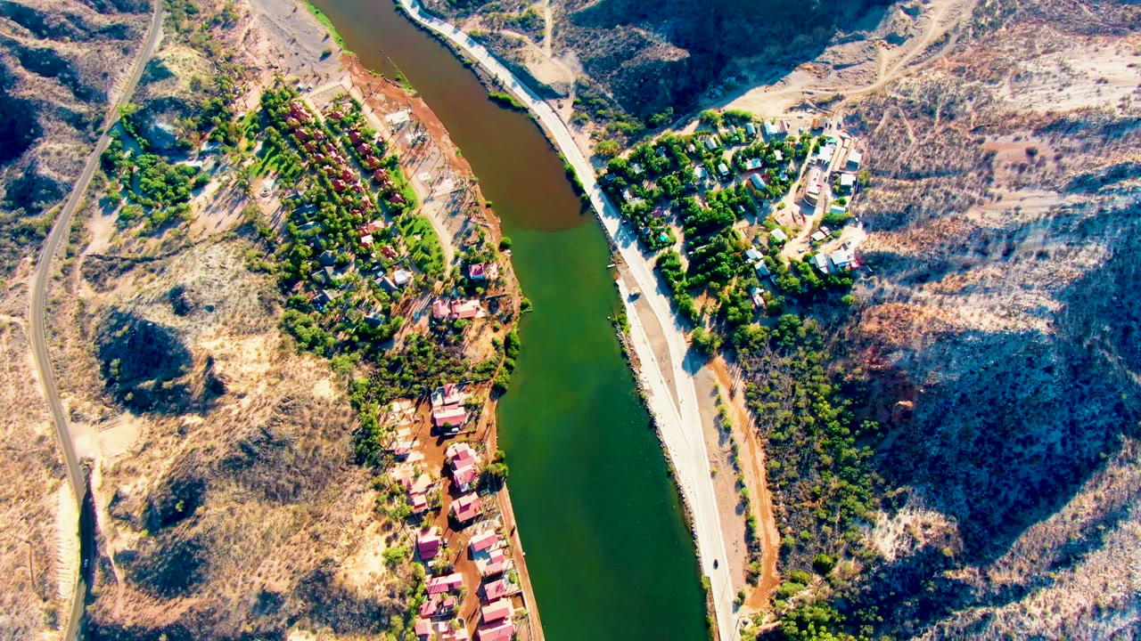 Overhead river bend with homes, road, trees, and arid hills