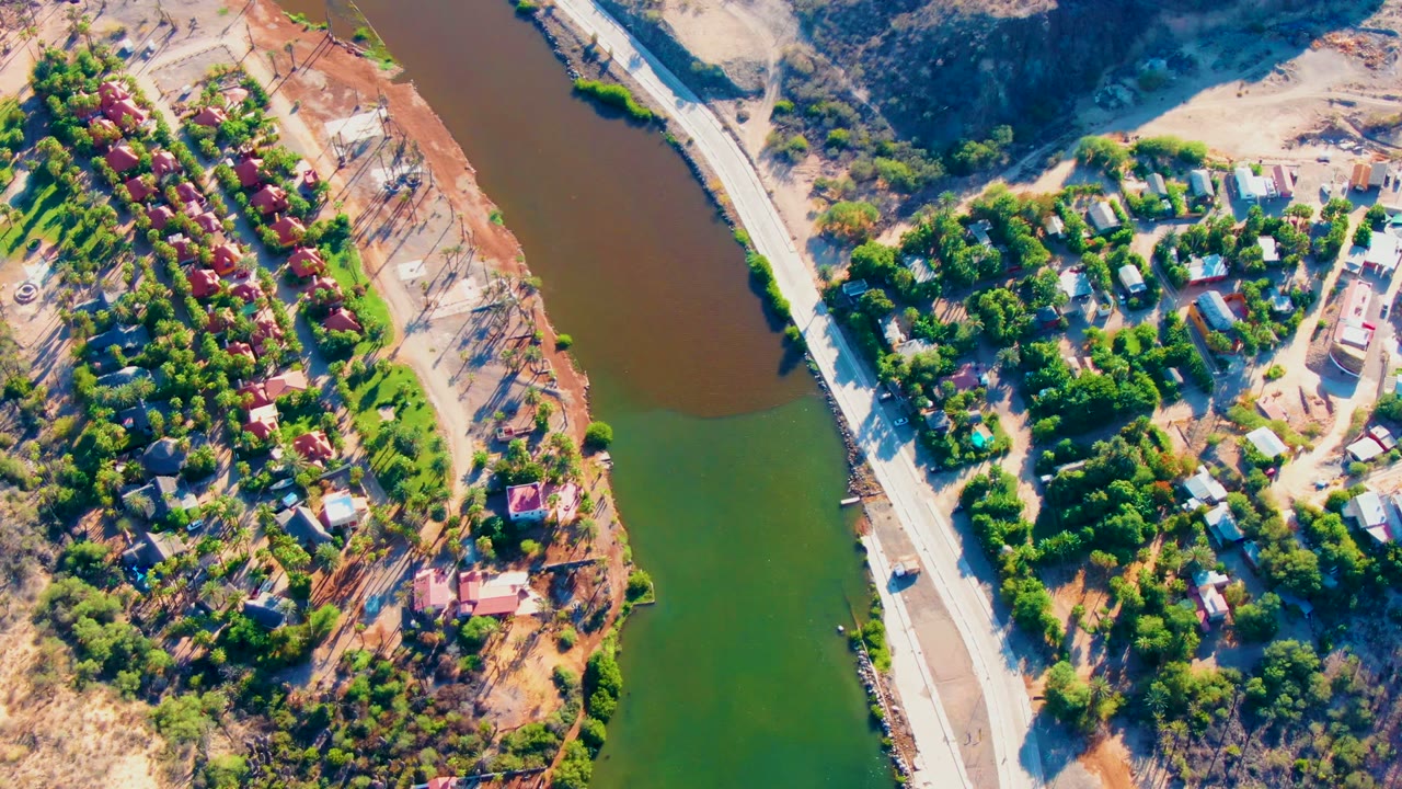 High aerial view of riverbank homes and a pale road.