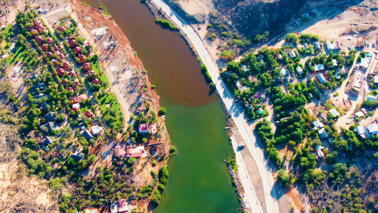 Aerial view of river bend, road bridge, green trees, houses, and brown hills.