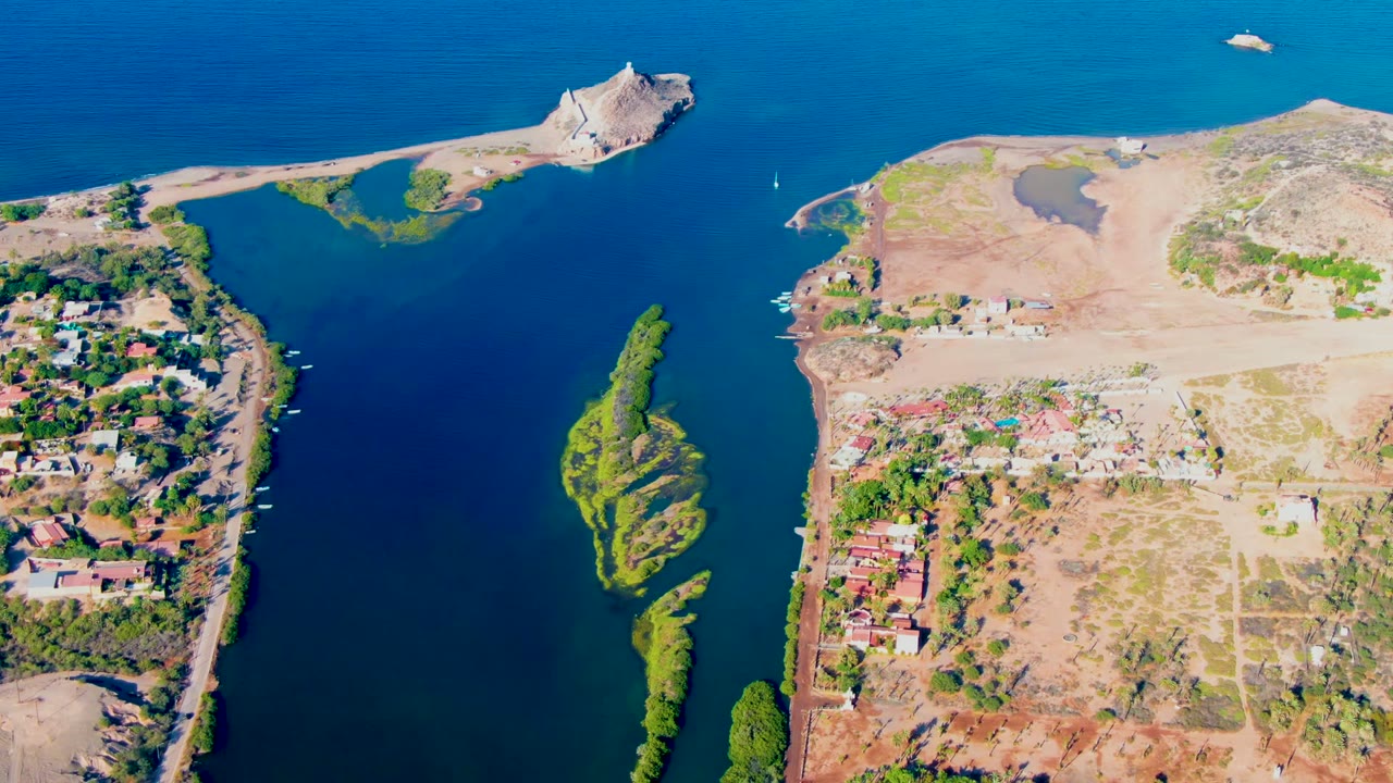 Aerial channel view with a small white boat near the upper water and buildings on both shores.