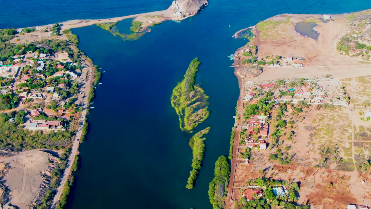 Drone view of a narrow island between deep blue water and shorefront homes.