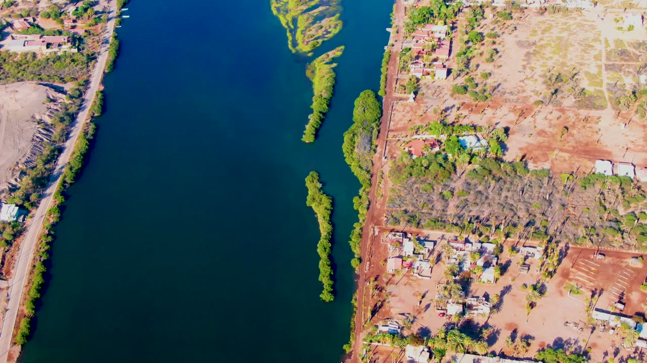 Drone view of river water, green island, and dry developed shore.