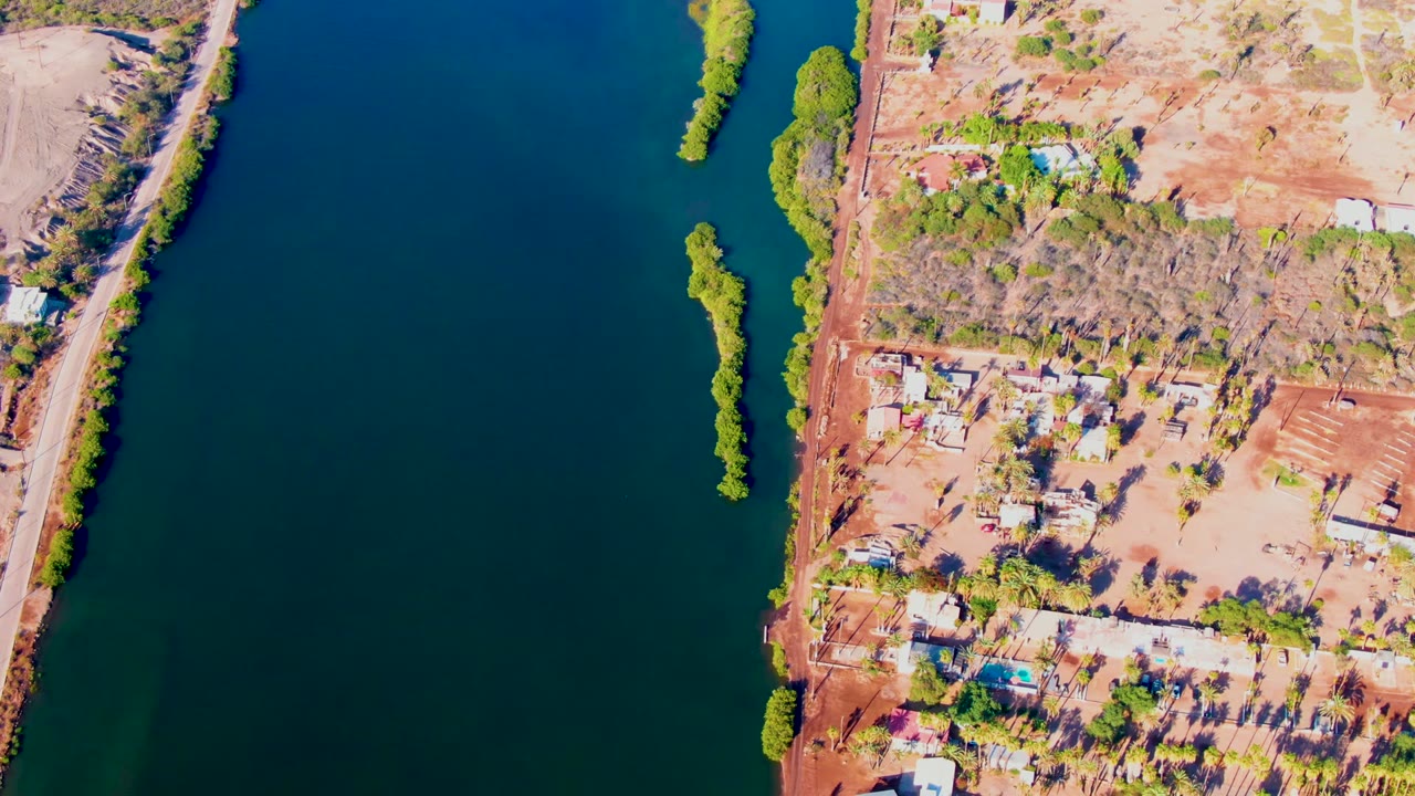 Aerial view of river water beside a dry bank with buildings and trees.