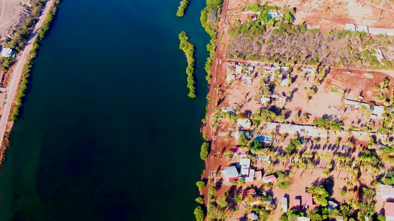 Drone view of riverbank homes beside dark blue water