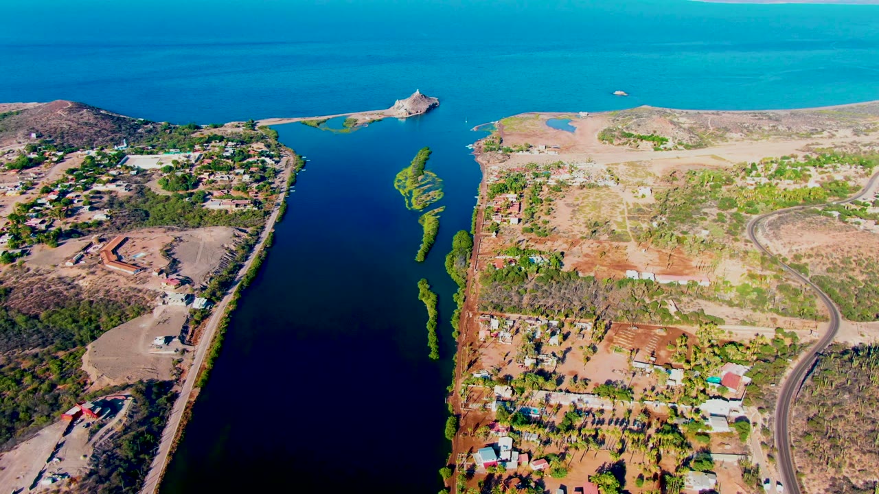 Aerial frame of dry coastal terrain, curving road, and blue water channel.