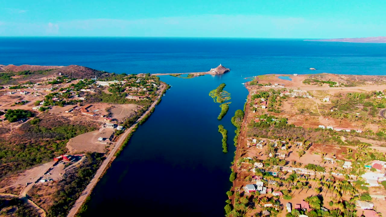 Aerial waterway view with roads, buildings, and dry terrain beside calm water.