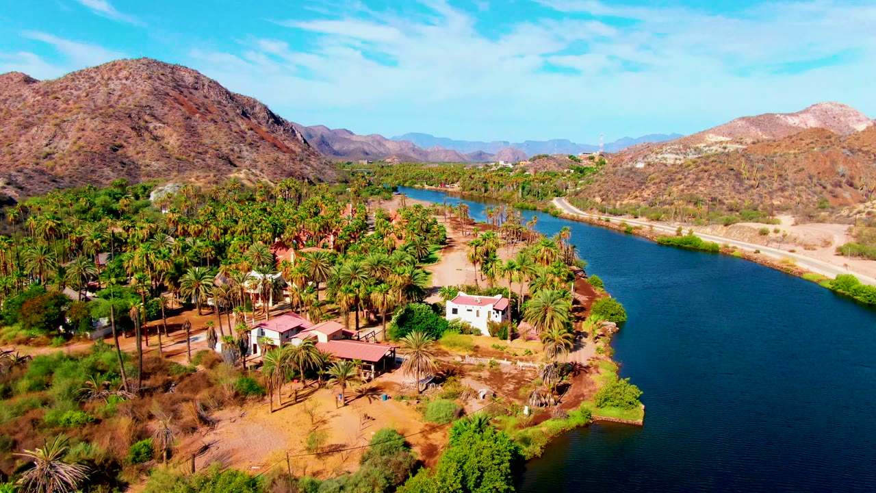 River curves past a palm grove and scattered buildings in a dry valley.