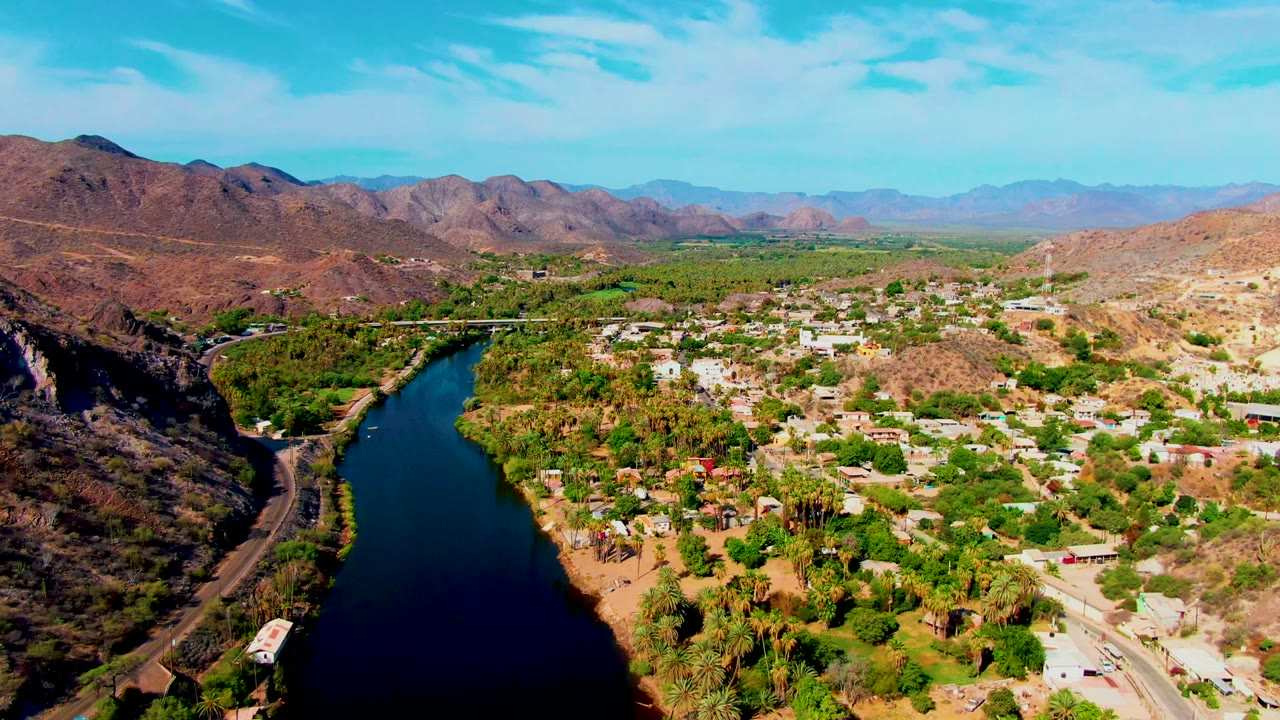 Wide drone view of river, roads, buildings, and arid mountains.