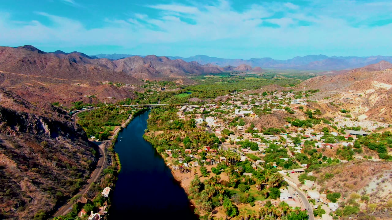 Drone view of river beside town and arid hills.