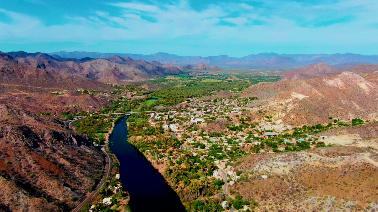 Wide aerial valley view with river on the left and settlement below desert hills.