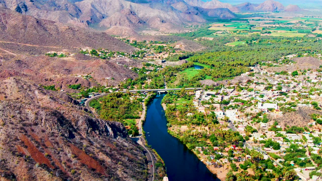 Drone view of blue river beside Mulege town and desert hills.