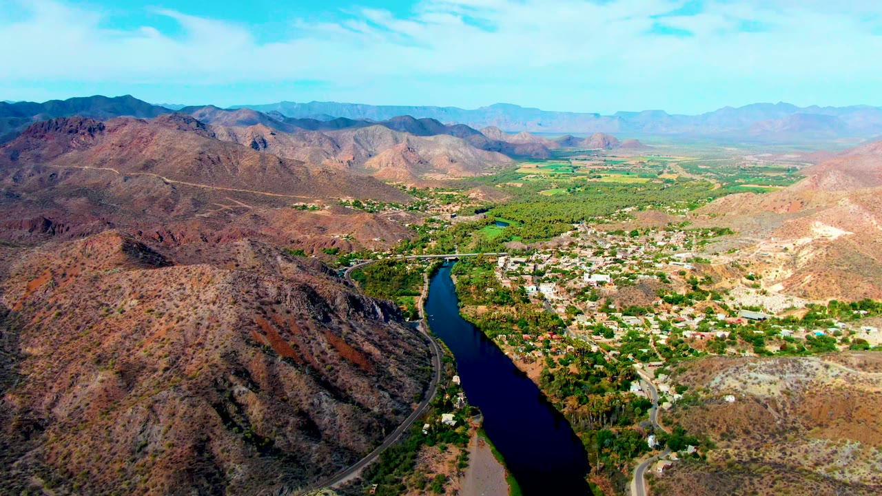 Aerial view of rocky hills beside a river and town under a bright sky.