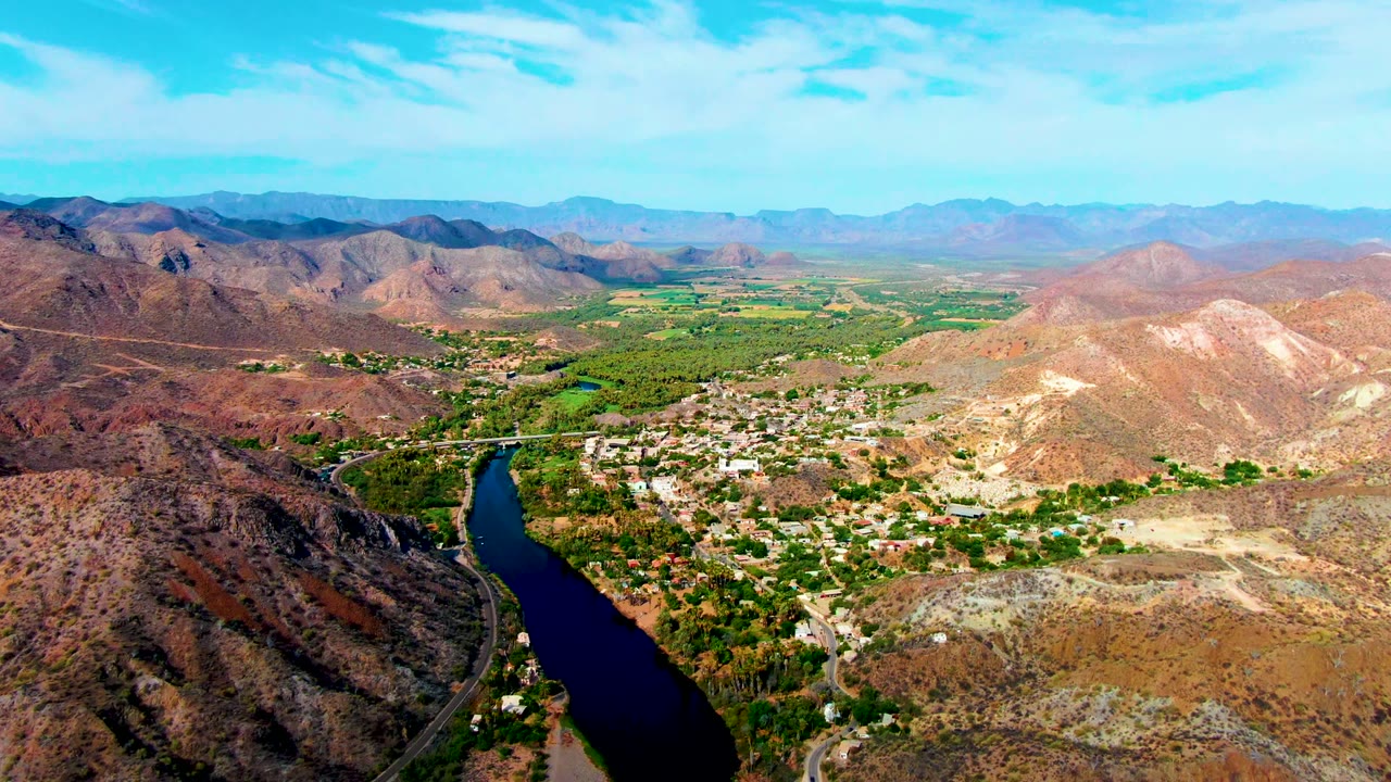 High aerial view of a winding river beside roads, trees, hills, and settlement.