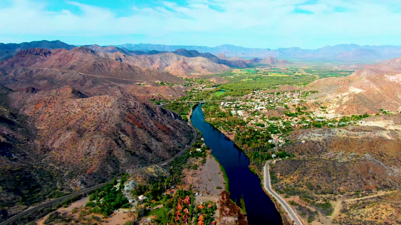 River valley aerial with road, village greenery, and desert hills.