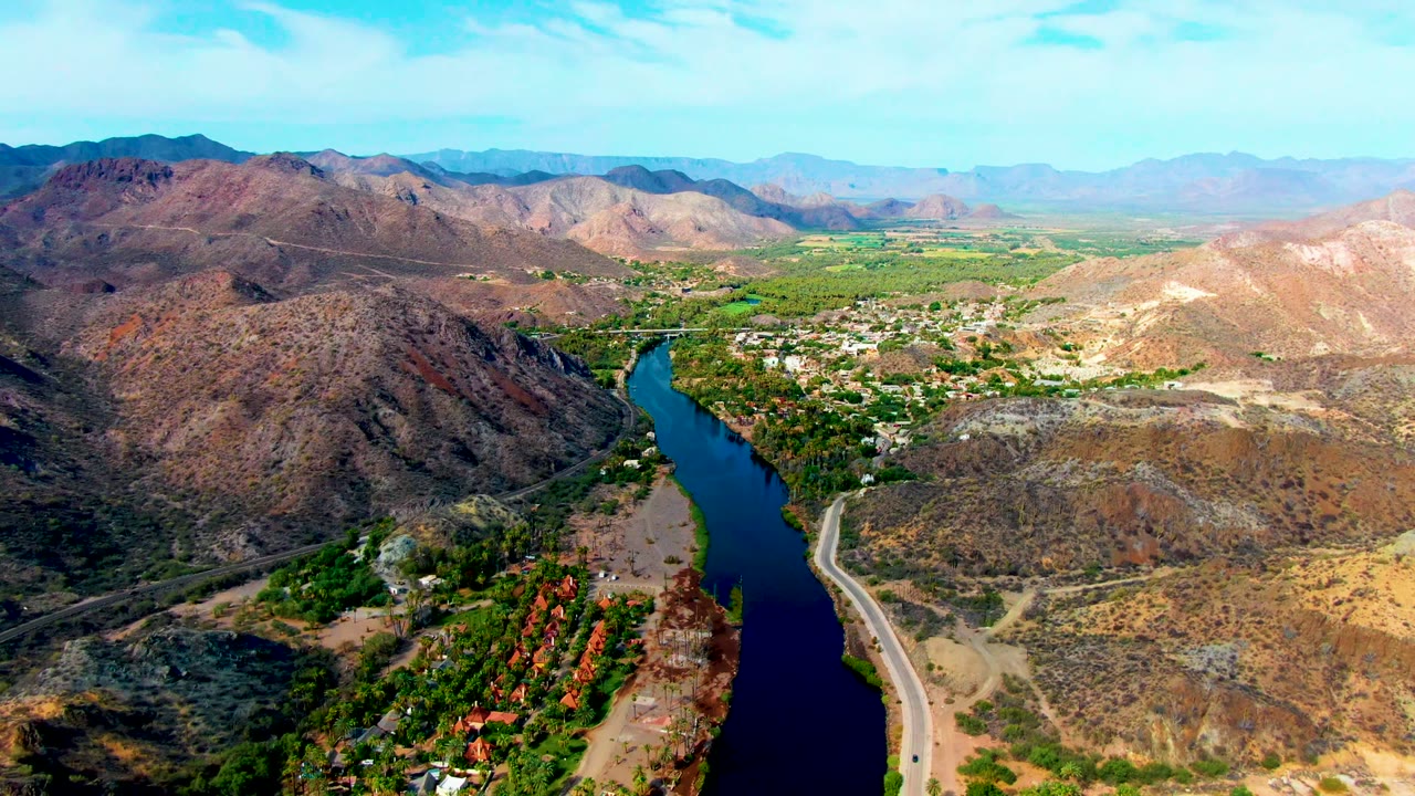 High drone view of a curving river below rugged hills and a road.