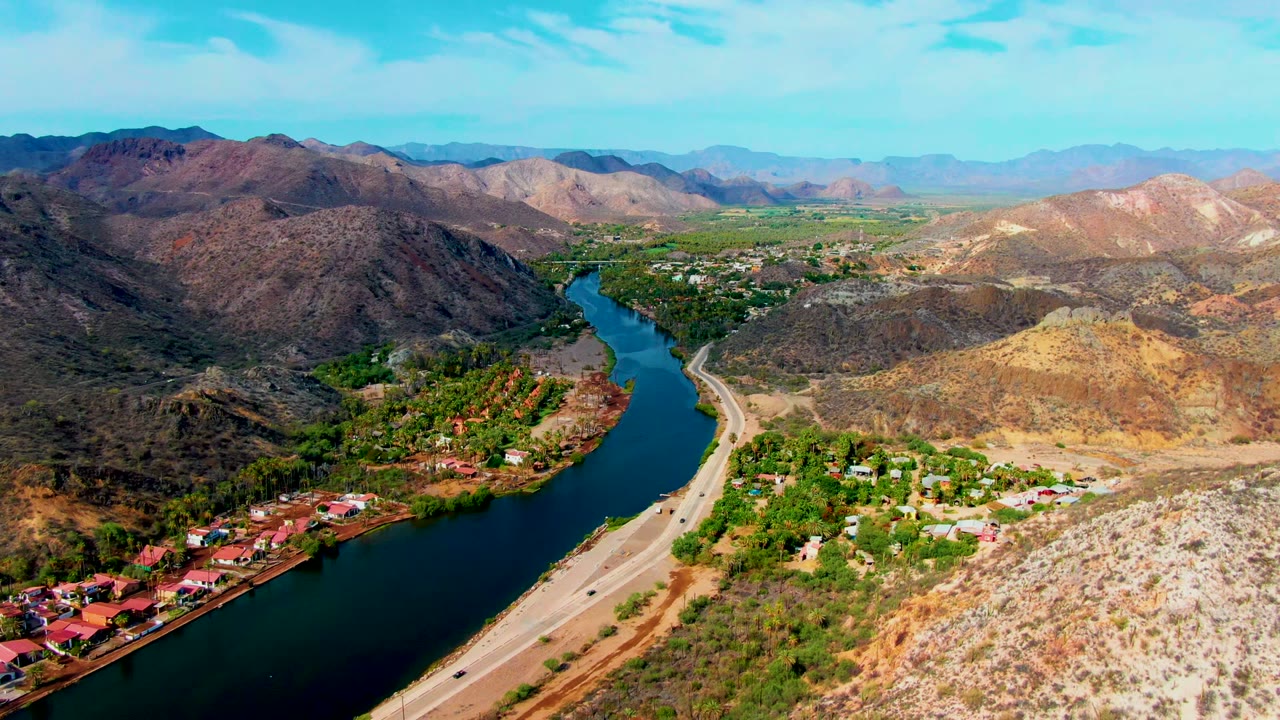 Aerial valley view with river bend, road, homes, and desert hills.