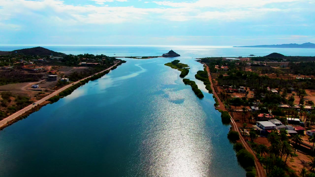 High view down a blue waterway with roads, palms, houses, and distant hills.